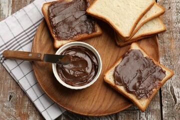 Tasty chocolate butter, slices of bread and knife on wooden table, top view