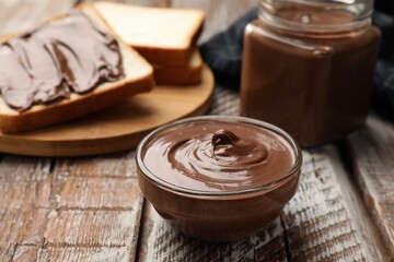 Tasty chocolate butter and slices of bread on wooden table, closeup