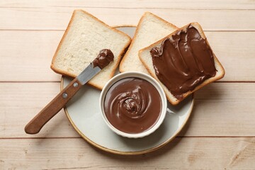 Tasty chocolate butter, slices of bread and knife on light wooden table, top view