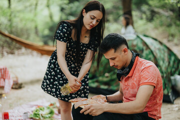 A young couple works together to prepare a meal outdoors while camping near the forest.