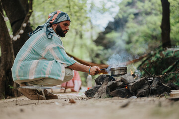 A man is preparing a meal over a campfire in an outdoors setting surrounded by greenery. The image...