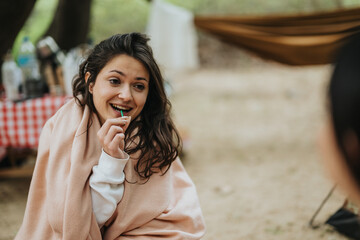 A young woman wrapped in a blanket enjoying a moment outdoors at a campsite. The natural...