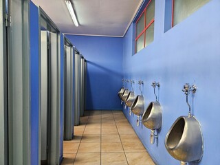 Row of urinals are lined up in a public restroom. The urinals are silver and are attached to the...
