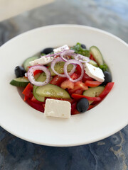 Vibrant and fresh Greek salad in a white bowl, featuring juicy tomatoes, crisp cucumbers, red onions, olives, and generous feta cheese. Healthy Mediterranean cuisine.