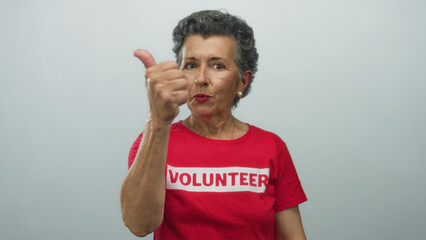 Senior woman with grey hair and red volunteer shirt gesturing enthusiastically against white...