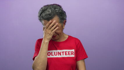 Senior woman volunteer with grey hair looks concerned against a purple background, touching her...