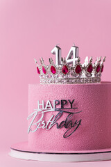 Beautiful luxury birthday anniversary cake for a girl with pink chocolate velvet coating decorated with silver crown and happy birthday topper. Pink background. Happy 14 years old celebration concept