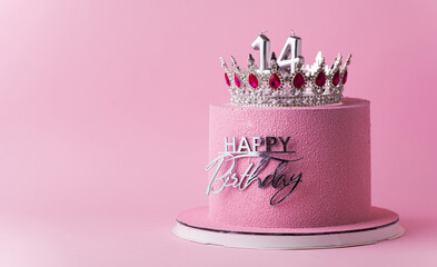 Beautiful luxury birthday anniversary cake for a girl with pink chocolate velvet coating decorated with silver crown and happy birthday topper. Pink background. Happy 14 years old celebration concept