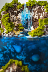 Beautiful birthday cake in the shape of an island decorated with chocolate edible mountains, greenery with waterfall. Tropical island cake surrounded with blue jelly ocean water