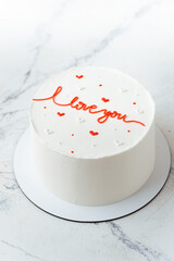 White chocolate cake decorated with red I love you text. Stylish cake for a beloved one. Valentine's cake on the white marble background