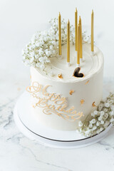 Beautiful white birthday cake decorated with golden candles and field  gypsophila flowers on the white background