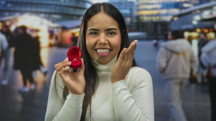 Woman smiling with engagement ring in red box on street evening lights city background facial expression.