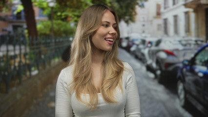 Blonde woman in white top touches cheeks on cobblestone street with parked cars; serenity contemplation joy peace.