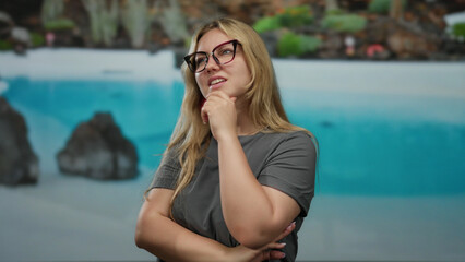 Woman pondering at outdoor resort by a pool in a serene setting with natural beauty, displaying thoughtful expression, sunlight reflecting off the clear water in background