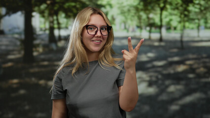 Woman celebrating outdoors in a park with cheerful expression, wearing glasses and a casual shirt,...