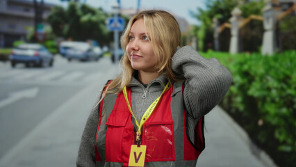 Fototapeta premium Woman wearing volunteer vest stands on urban street in city with vehicles in background.