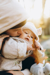 Happy father hugging and kissing cute baby son in soft evening light in autumn woods. Fatherhood. Stylish man with adorable child in cozy warm sweaters embracing in fall park