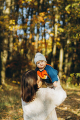 Happy mother playing with cute baby son in autumn woods. Motherhood. Stylish woman with adorable child in cozy warm sweaters having fun and relaxing in fall park