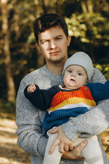 Happy father hugging cute baby son in autumn woods. Fatherhood. Stylish man with adorable child in cozy warm sweaters having fun and relaxing in fall park