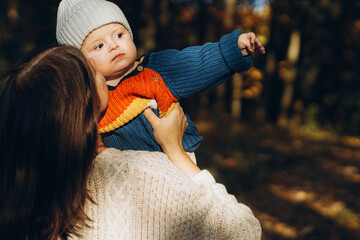 Happy mother hugging and kissing cute baby son in autumn woods. Motherhood. Stylish woman with adorable child in cozy warm sweaters embracing and relaxing in fall park