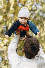 Happy father playing with cute baby son in autumn woods. Fatherhood. Stylish man with adorable child in cozy warm sweaters having fun and relaxing in fall park