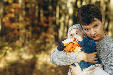 Happy father hugging cute baby son in autumn woods. Fatherhood. Stylish man with adorable child in cozy warm sweaters embracing and relaxing in fall park