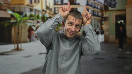 Man making funny gesture with fingers resembling horns on busy urban street.