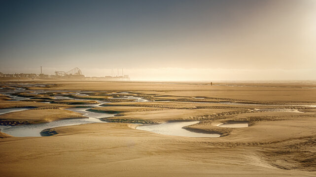 Expansive sandy beach with tidal pools and distant amusement park at sunrise