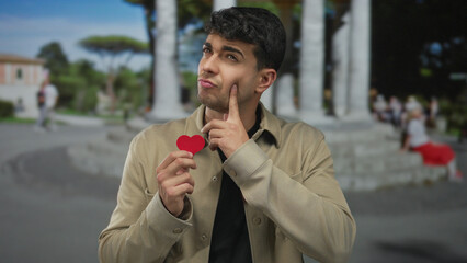 Man holds heart and think about plaza memories while love sparks red paper token by young hispanic...