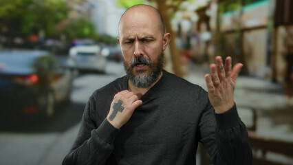 Man with beard standing on urban street outdoors appearing hot and uncomfortable in the summer heat.