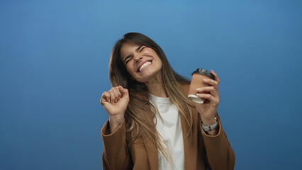 Woman holding coffee cup, celebrating on isolated blue background, embodying energy, excitement,...