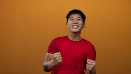 Young man expressing emotions against an isolated orange background, emphasizing excitement,...