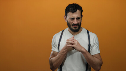 Hispanic man with beard stands against vibrant orange background, wearing white shirt and...
