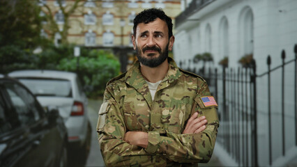 Man with beard wearing military uniform stands outdoors in city street with cars, showcasing a...