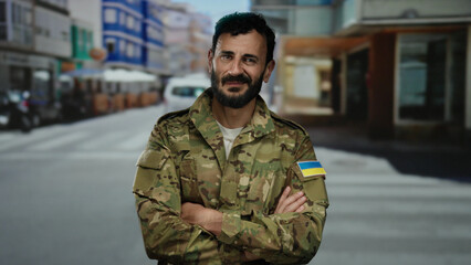 Man in military uniform with ukrainian flag patch stands confidently on a city street outdoors.