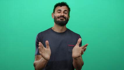 Hispanic man with beard clapping hands against vibrant green background, wearing casual t-shirt,...