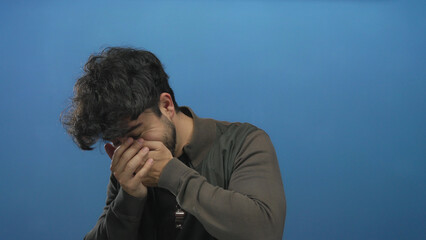 Young hispanic man with beard laughing and covering face against blue background showing joy and happiness.