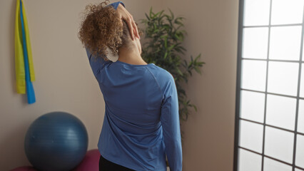 Woman stretching in gym interior with exercise ball and resistance bands, showcasing athletic...
