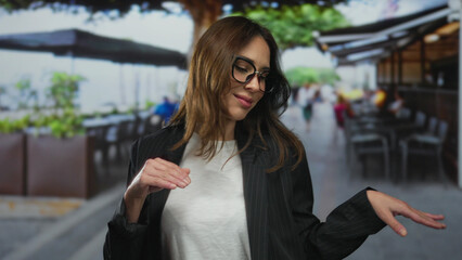 Woman smiling on outdoor terrace, relaxed and enjoying city life in casual attire with vibrant street background and coffee, embodying youthful energy and joyful demeanor.