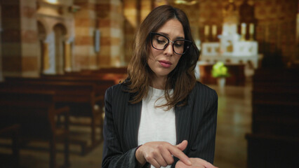 Young hispanic woman in glasses gestures for money inside a church with ornate architecture and...