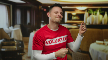 Man in restaurant wearing volunteer shirt smiling and dancing joyfully indoors showing his tattoos...