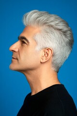 Fototapeta premium A modern and graceful man smiling naturally. Blue solid background. Idea of style for aging men. Modish men's two-block cut haircut - midlife arabian man with middle hair.