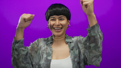 Woman smiling with arms raised against vibrant purple background, expressing joy and excitement,...