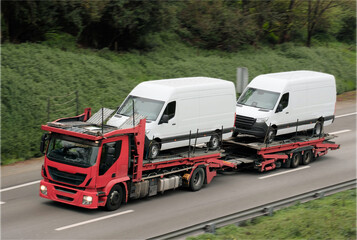 Red Car Carrier Transporting Two White Cargo Vans on Highway