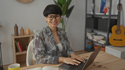 Woman using laptop in living room with bookshelves guitar surrounded by plants wearing glasses and...