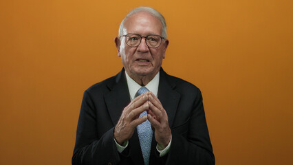 Senior man in a suit isolated against an orange background, displaying a thoughtful demeanor in a...