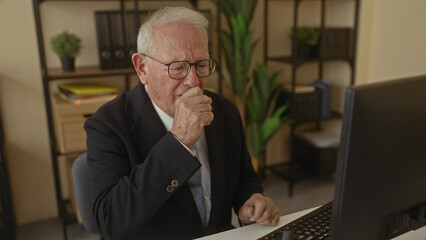 Senior man in suit sitting at desk in office appears unwell touching throat and coughing at...