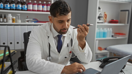 Young man in hospital clinic recording voice message on phone, wearing white lab coat, working at...