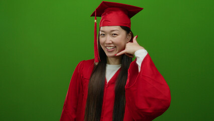 Woman celebrating graduation in red cap and gown against isolated green background, posing...