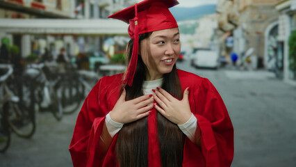 Woman in red graduation gown smiling outdoors in urban street setting showcasing joy and...